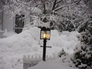 A classic carriage lamp sits at the end of a walkway in the snow.